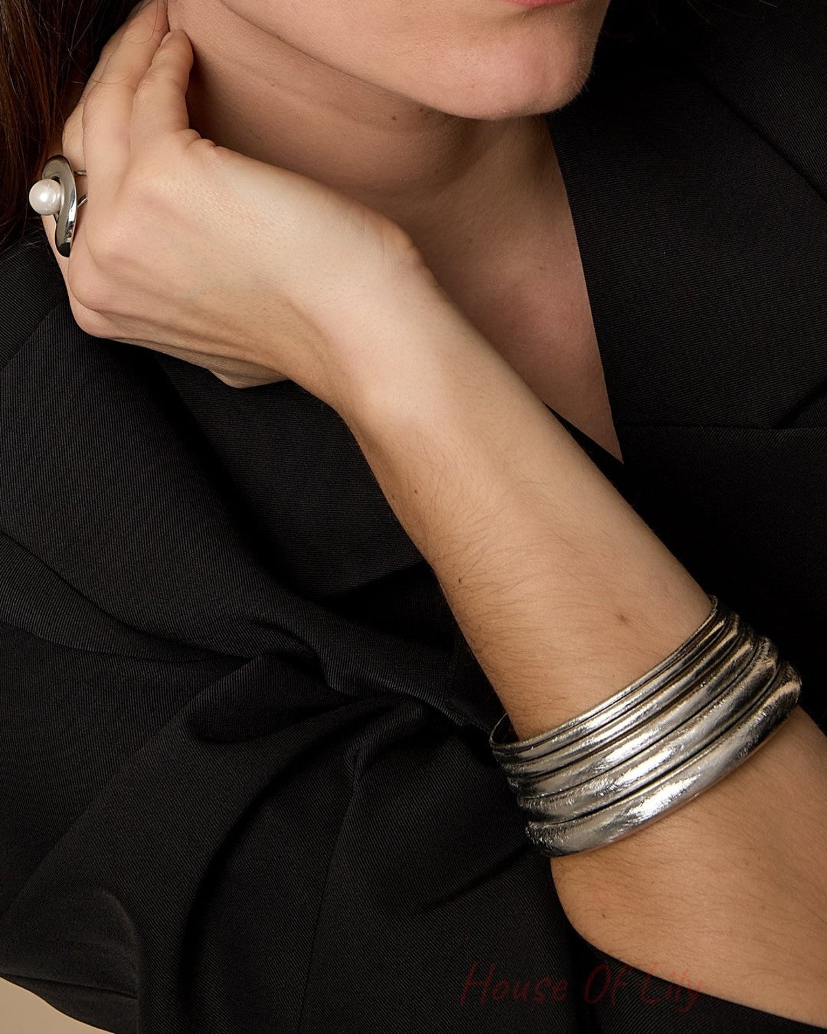 Woman wearing multiple textured silver bangles on wrist paired with black outfit