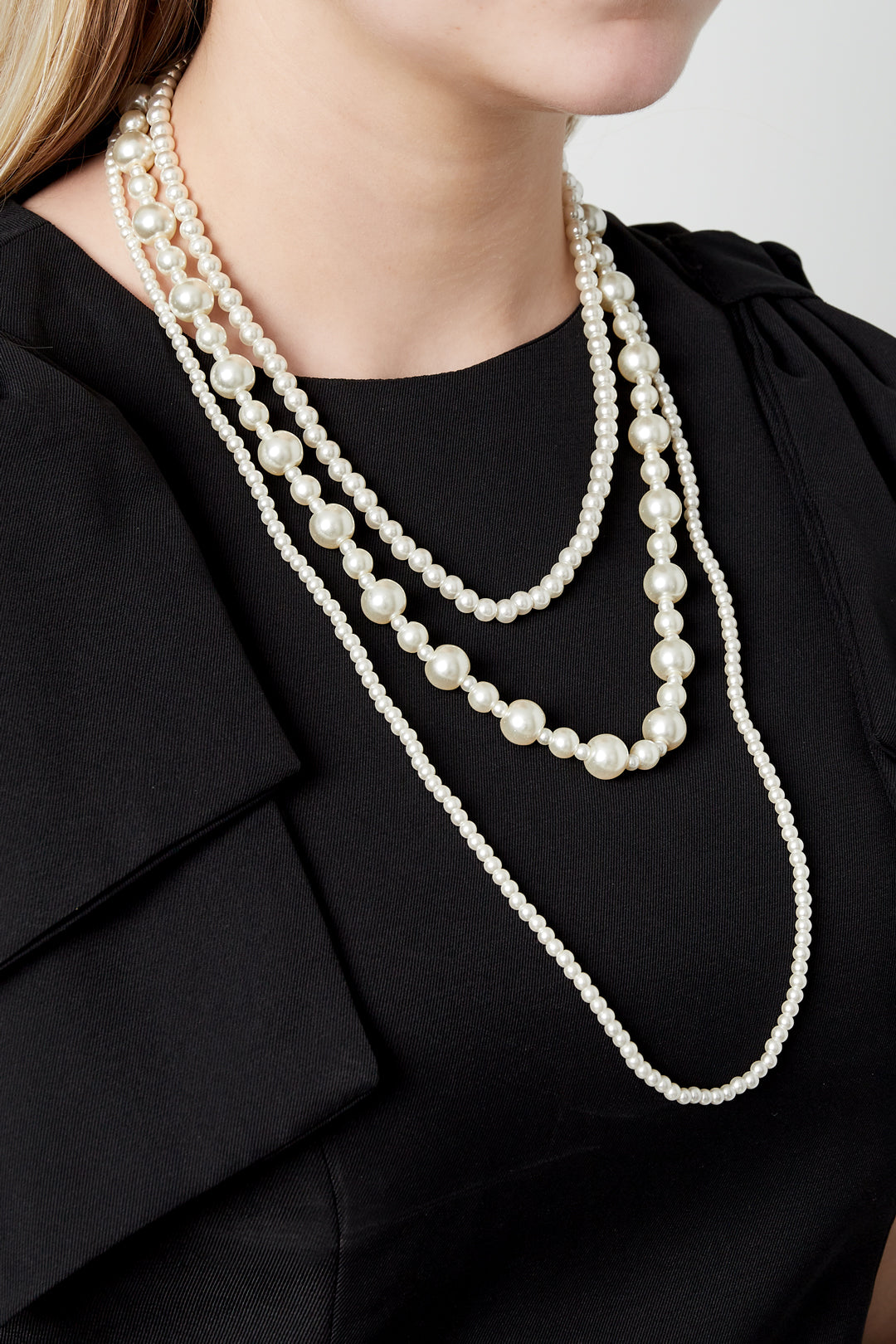 Close-up of a woman wearing a layered pearl necklace with varying pearl sizes over a black top
