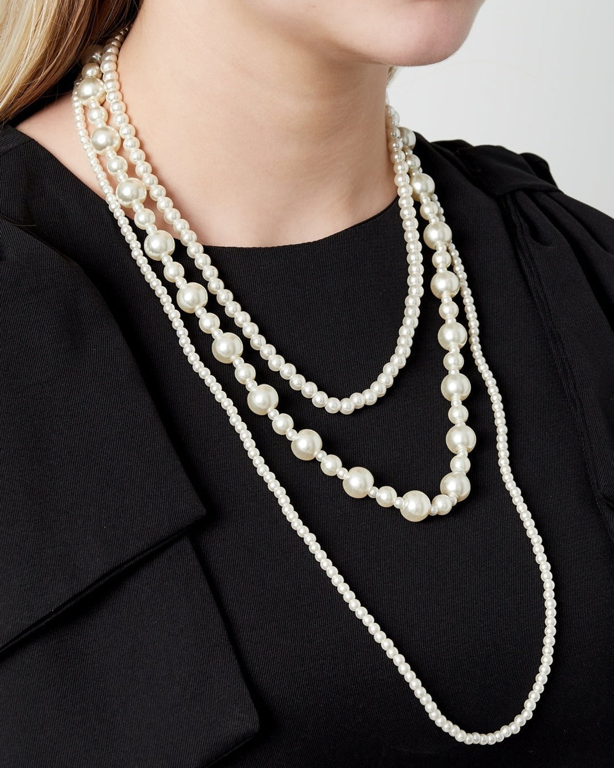 Close-up of a woman wearing a layered pearl necklace with varying pearl sizes over a black top