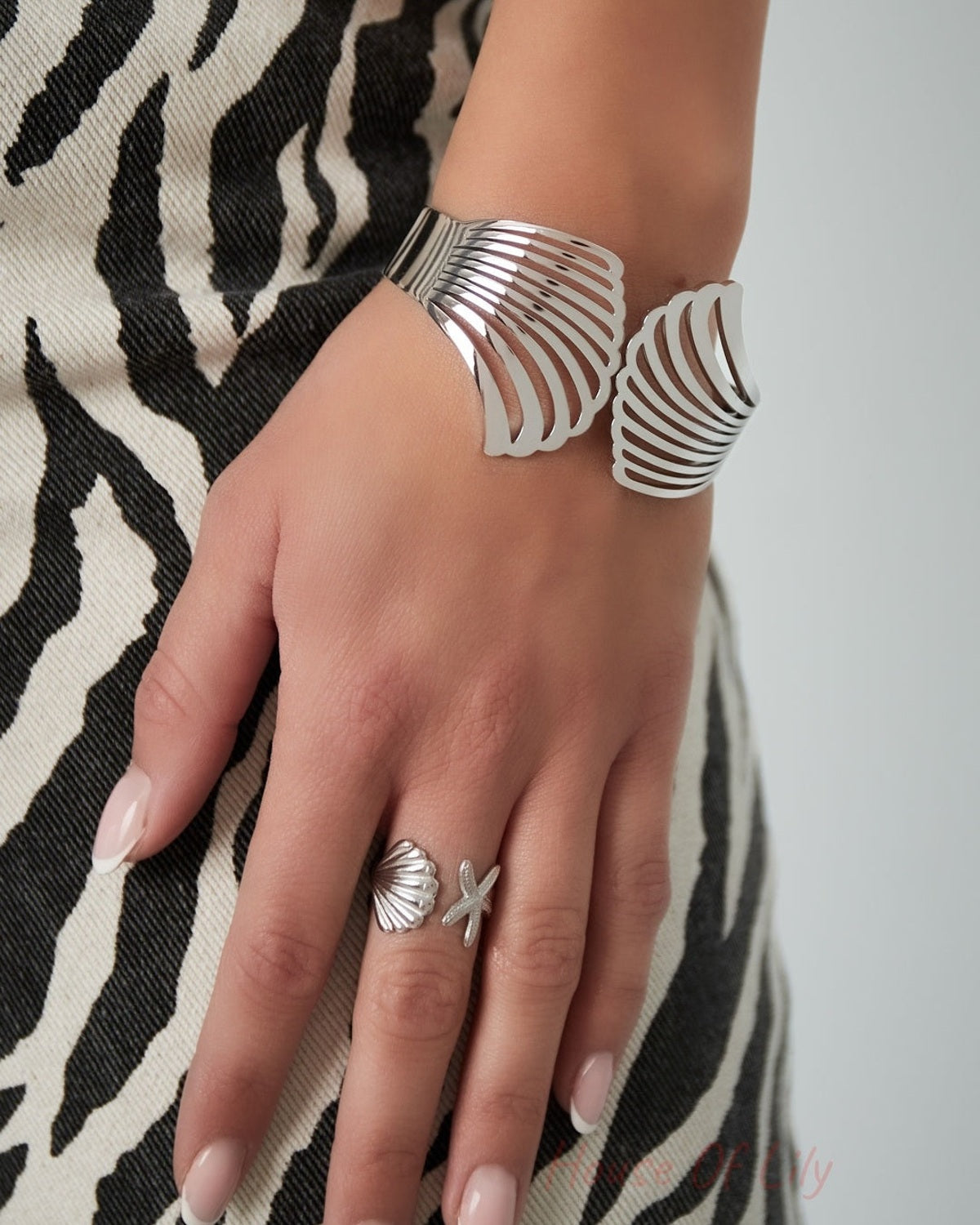 Close-up of a woman wearing silver shell design cuff bracelet and matching shell-and-starfish ring with zebra print dress