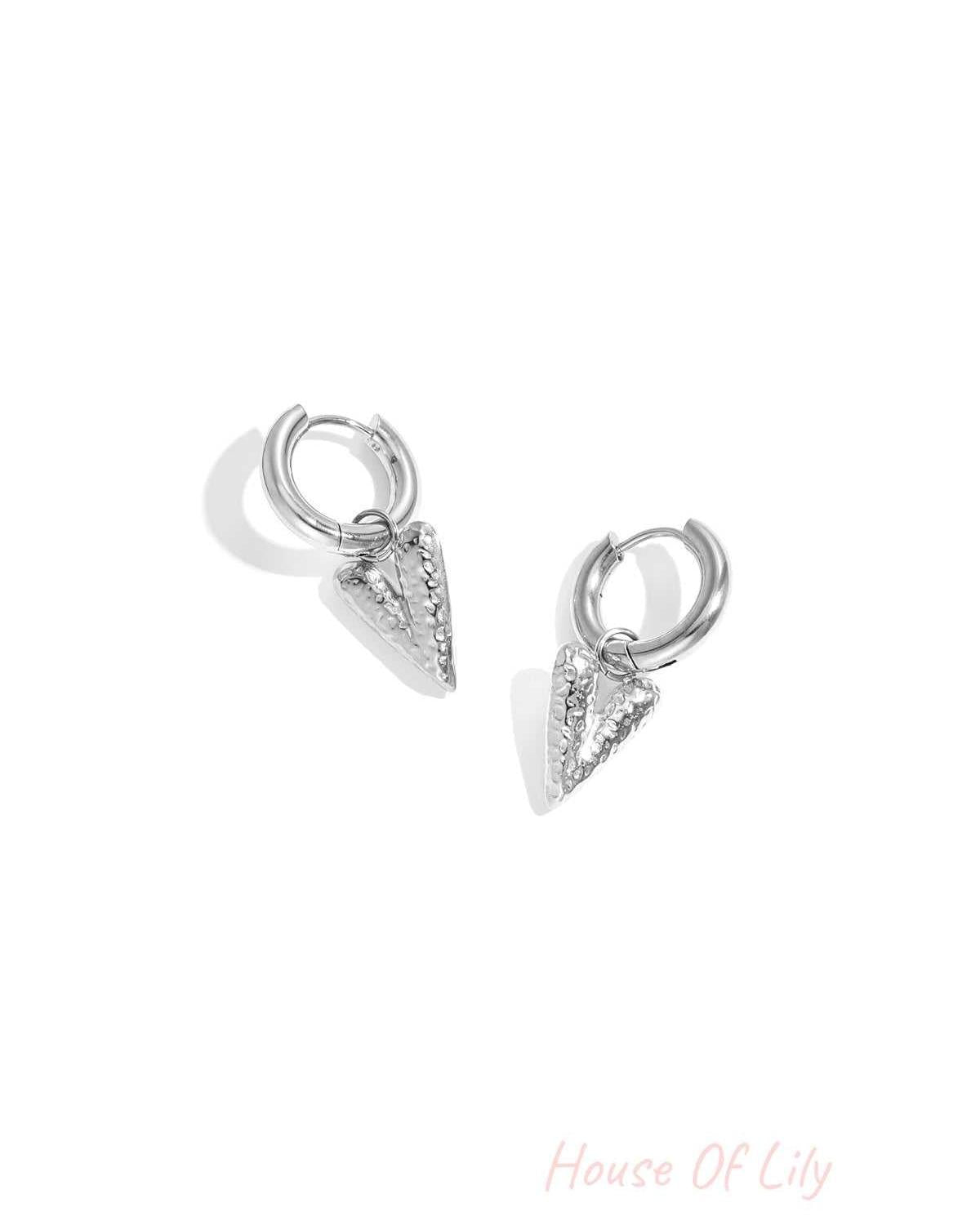Pair of silver hoop earrings with textured heart-shaped pendants displayed on white background