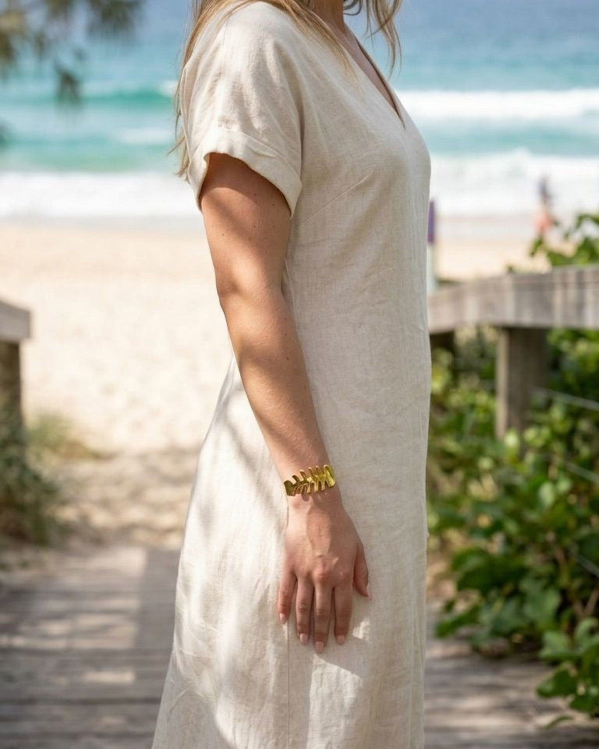 Model on outdoor beach setting wearing a delicate gold fishbone cuff bangle on her wrist in natural daylight.