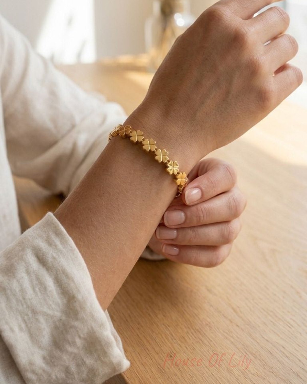 Delicate gold-tone stainless steel bangle with linked four-leaf clover motifs on a textured wooden surface, emphasizing its polished finish and intricate design for everyday style.