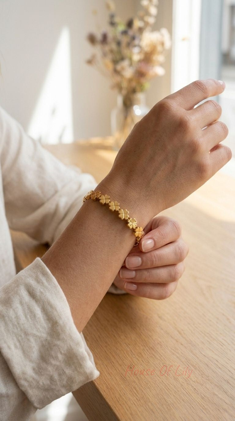 Delicate gold-tone stainless steel bangle with linked four-leaf clover motifs on a textured wooden surface, emphasizing its polished finish and intricate design for everyday style.