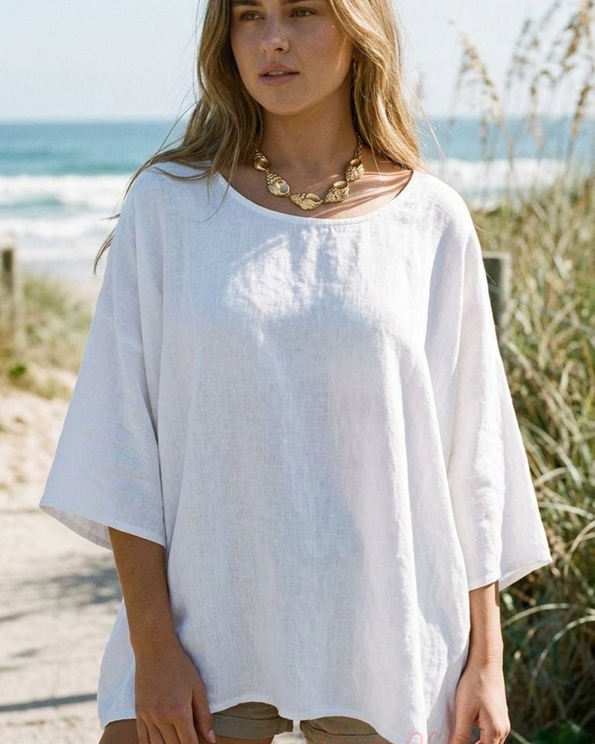 Full-body shot of a woman wearing the Golden Siren Energy necklace outdoors on a sunny day, with a boho beach outfit and coastal background.
