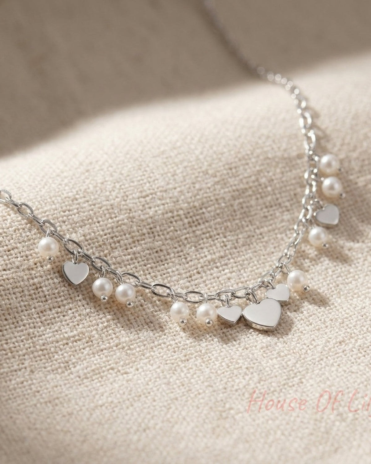 High-resolution macro image of the Hearts & Pearls Pendant Necklace, showcasing tiny heart-shaped charms and faux pearls on a soft fabric background with fine craftsmanship details.