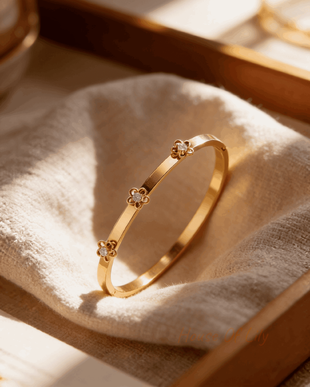 Gold bangle bracelet featuring three delicate floral-shaped motifs with central clear rhinestones on a fabric background.