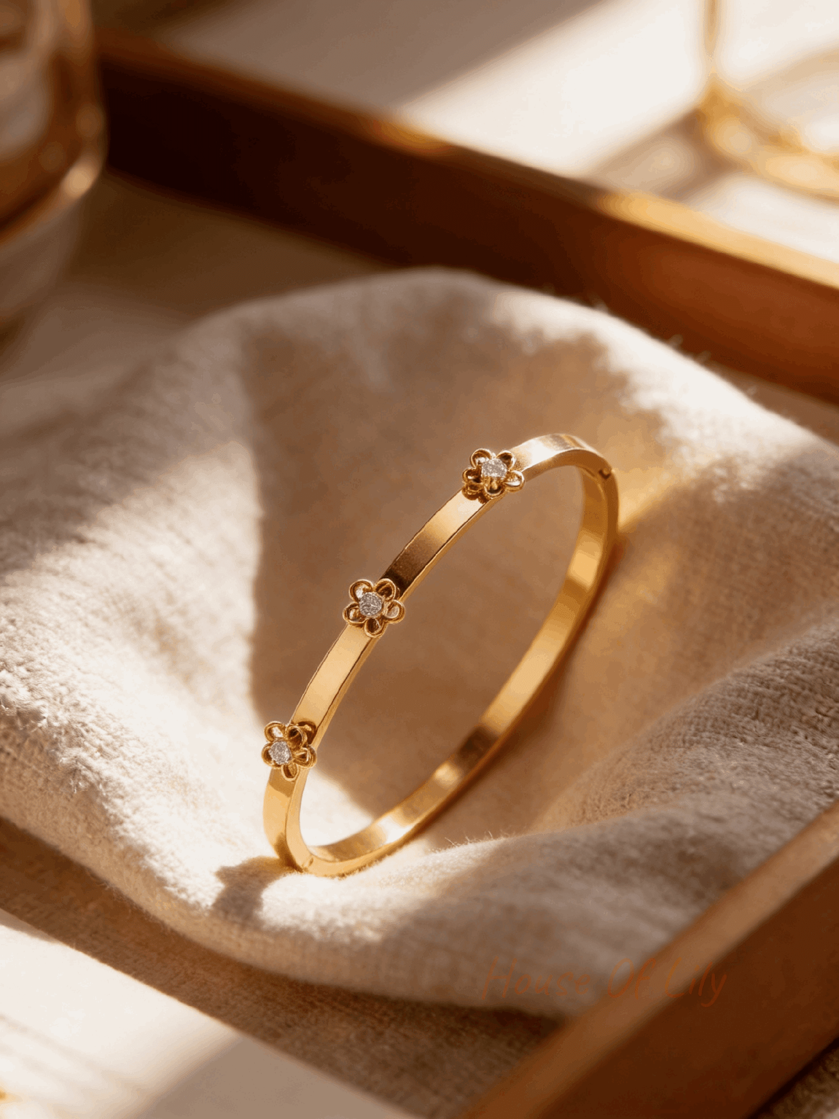 Gold bangle bracelet featuring three delicate floral-shaped motifs with central clear rhinestones on a fabric background.
