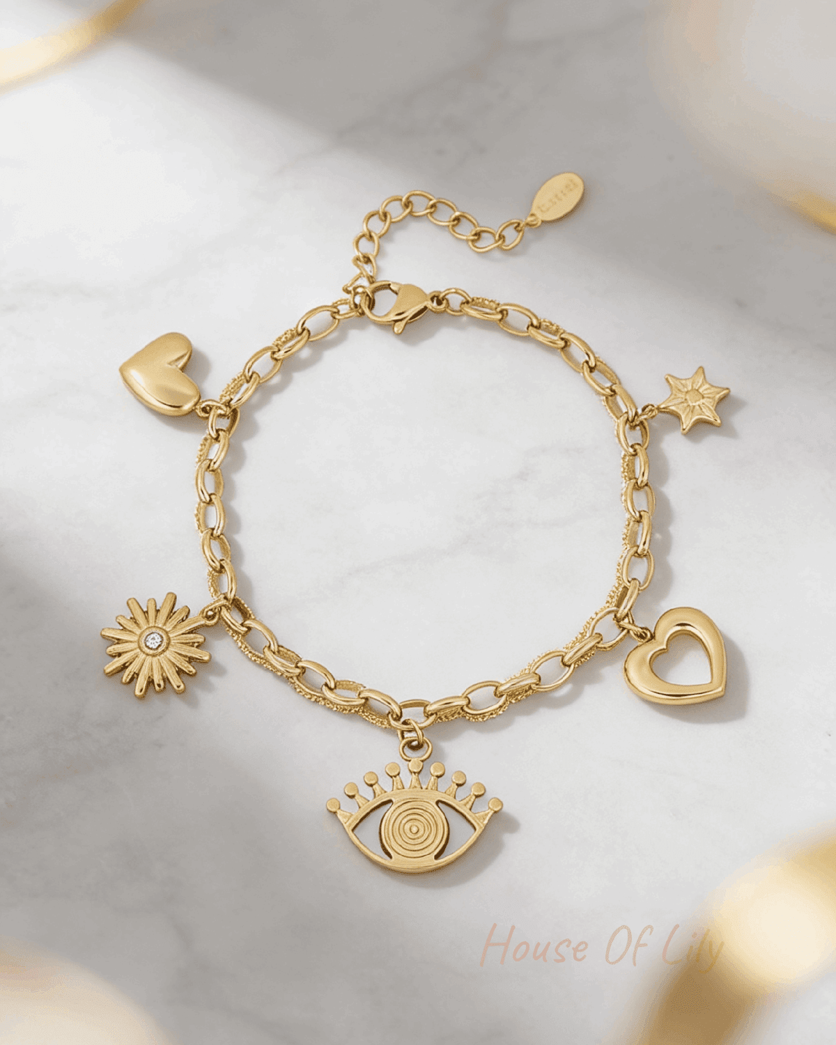Gold charm bracelet featuring evil eye, heart, sun, and star charms on a textured link chain against marble.