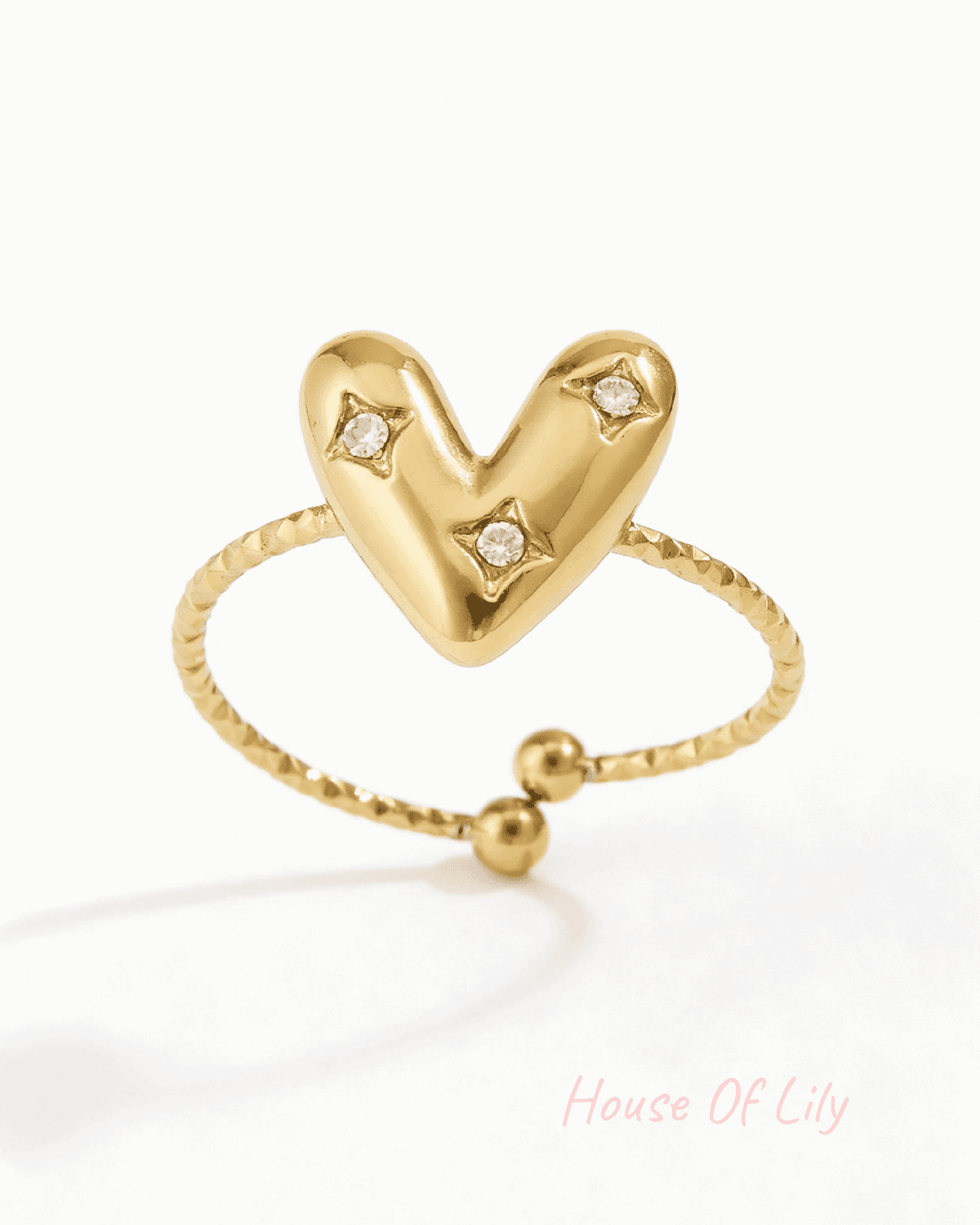 Gold-tone adjustable ring featuring a puffy heart center with three small inlaid crystals on a textured band.
