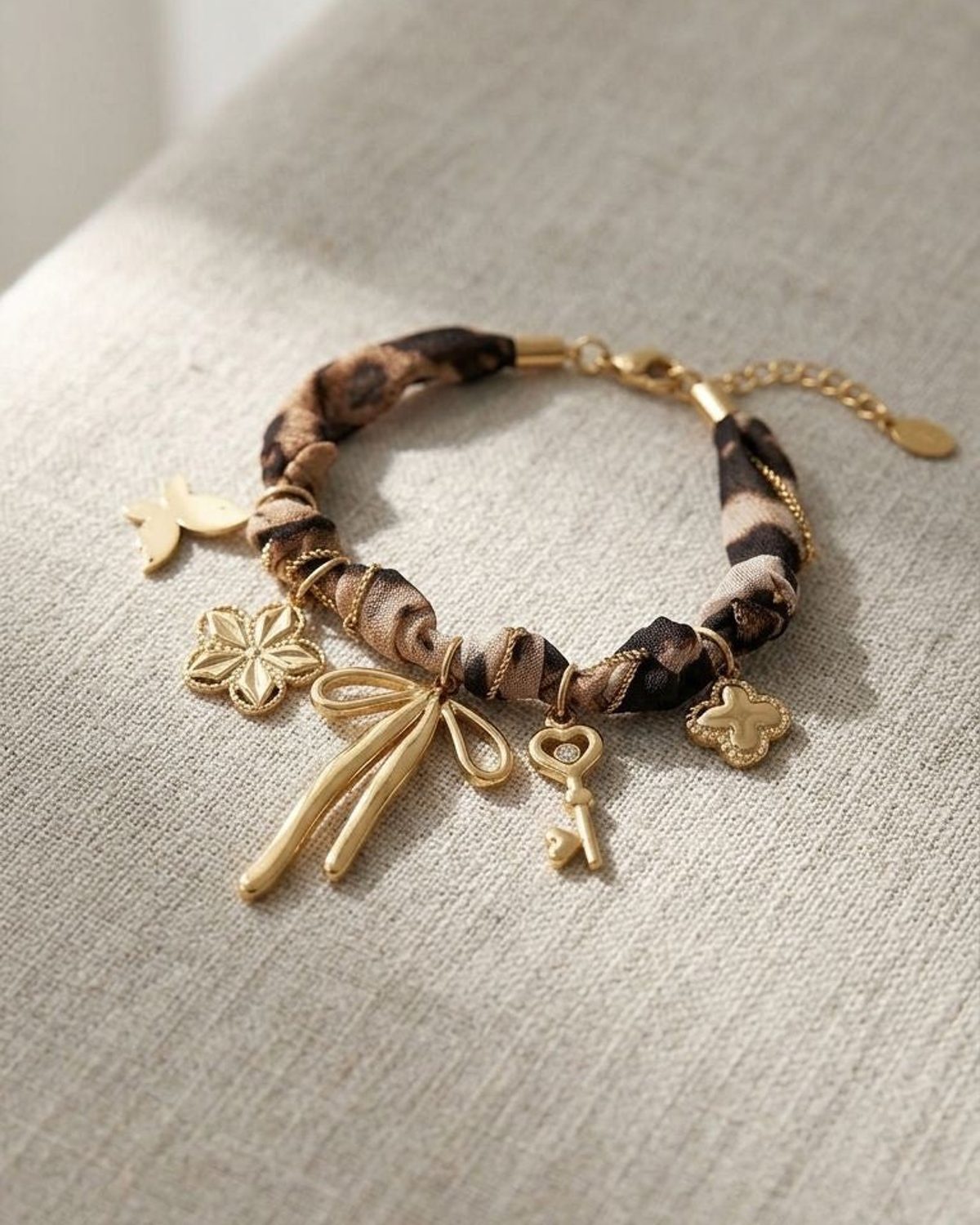 Close-up of leopard charm bracelet with fabric band and gold charms on neutral textured surface