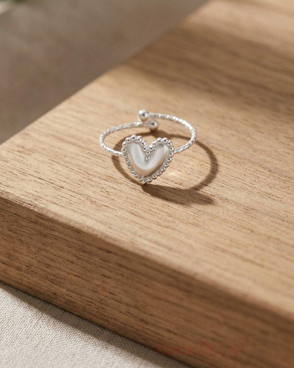 Close-up of the small stainless steel 'Main Character Energy' ring on a wooden surface, highlighting its minimalist design and subtle shimmer.