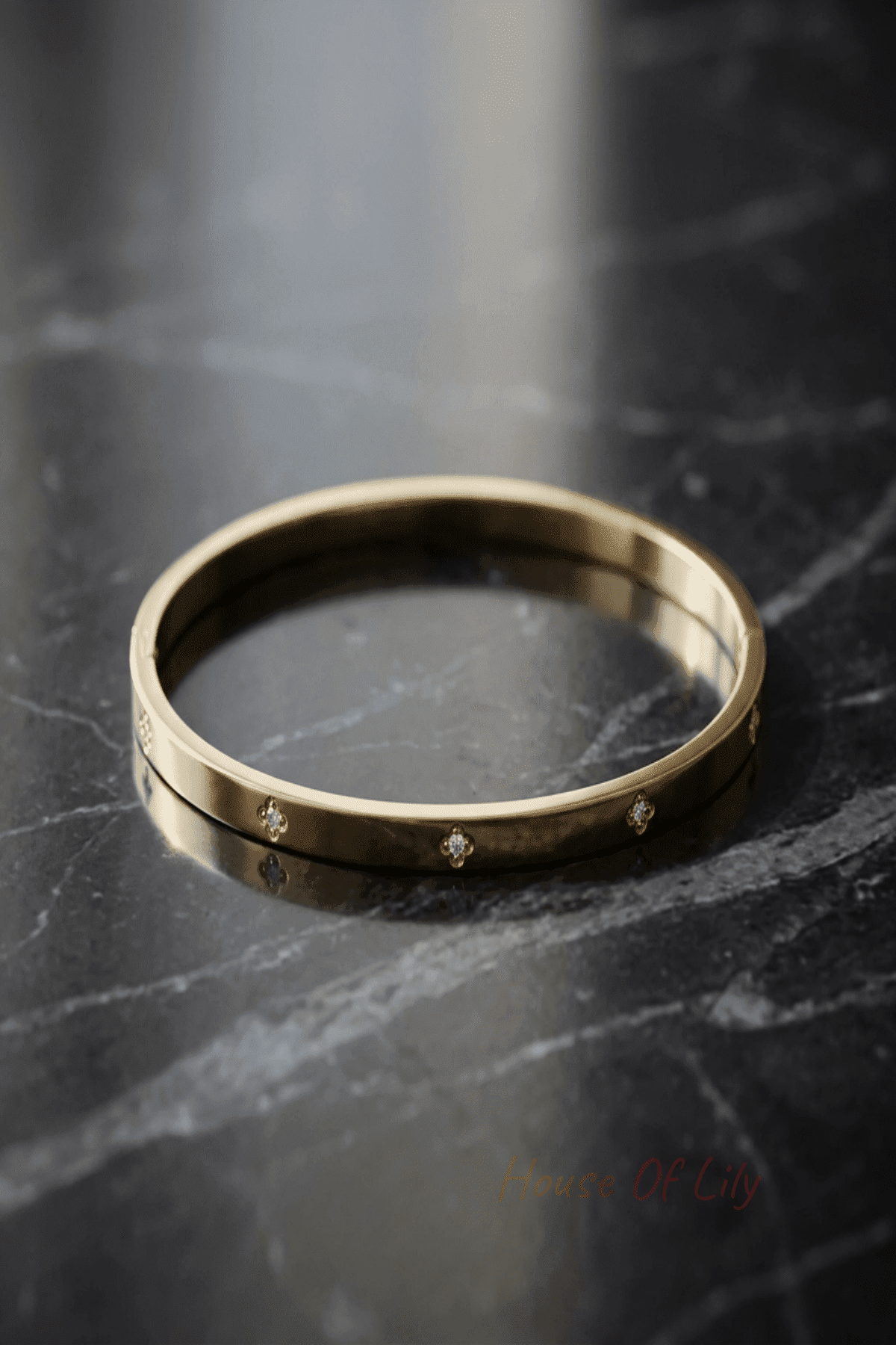 Close-up of a tiny, minimalist gold bangle with sparkling stones on a dark marble surface, emphasizing delicate design and fine details.