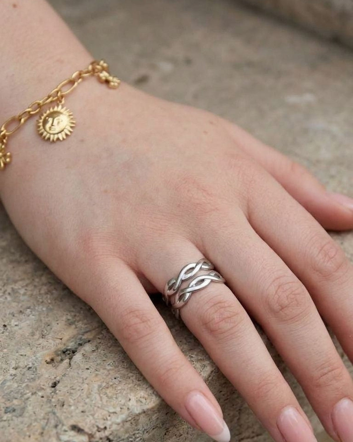 Small stainless steel ring with a double swirl design displayed on matte stone, captured from above with natural daylight emphasizing its polished finish.