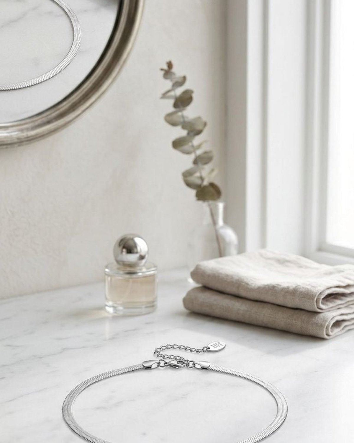 Minimalist silver-plated stainless steel necklace resting on white marble with natural window light, emphasizing its high-shine and elegant design.