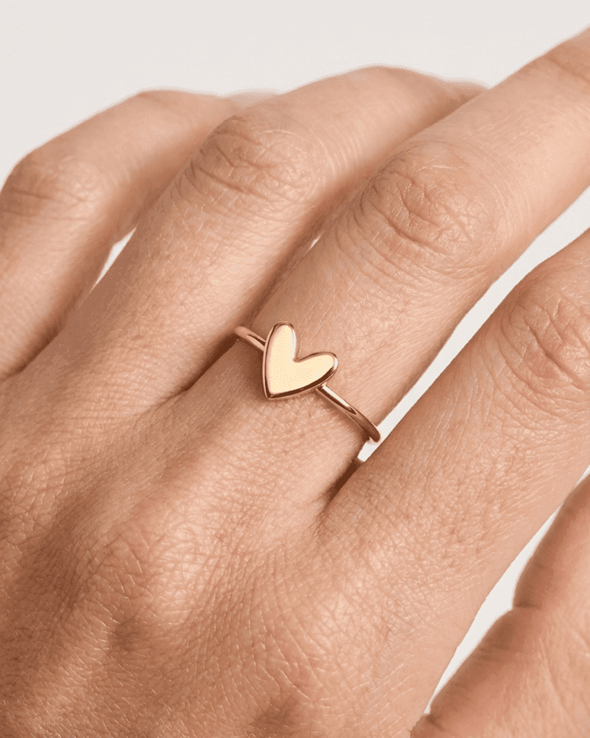 Minimalist gold band ring featuring a small, polished, solid heart-shaped charm on a slender finger.