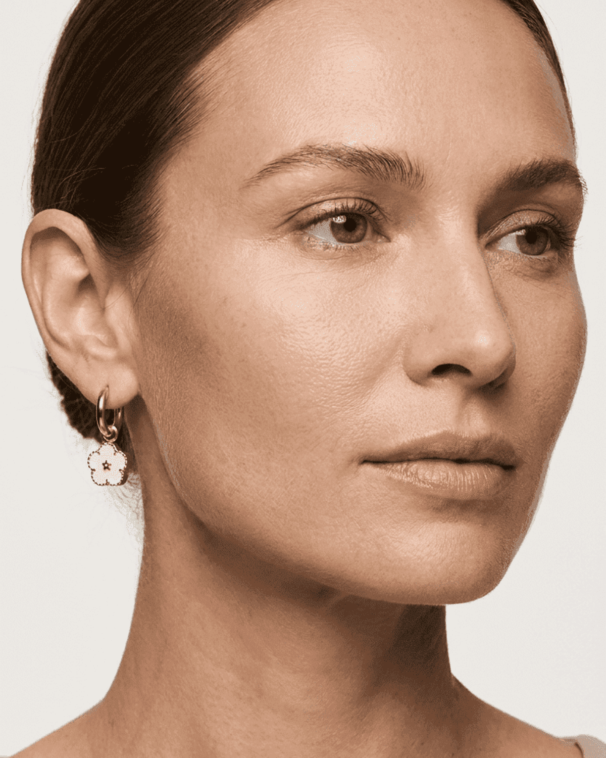 Model wearing gold hoop earrings with small, light pink soft enamel flower charms.