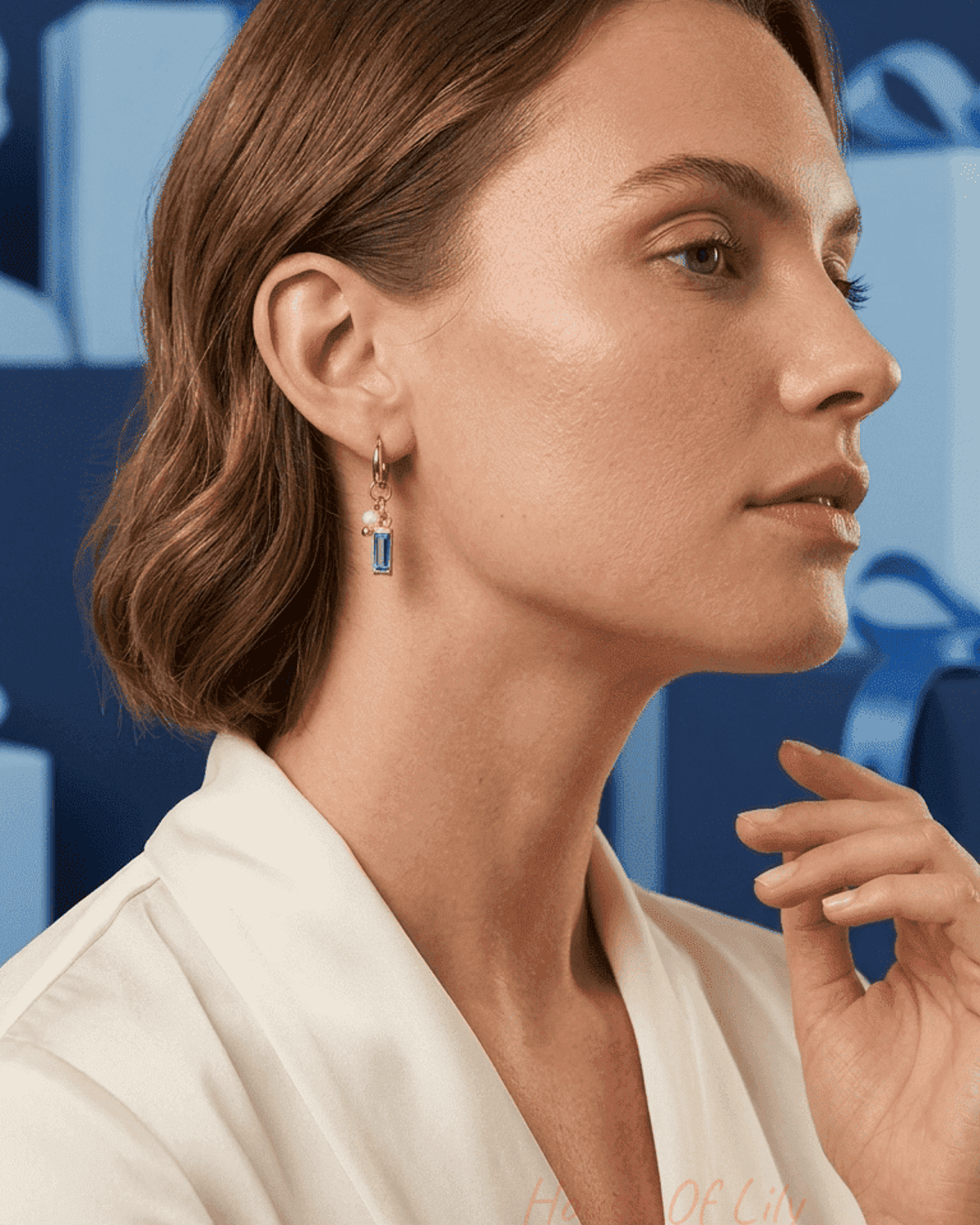 Dainty gold charm hoop earring with a small pearl and rectangular blue gemstone, worn by a woman in profile.