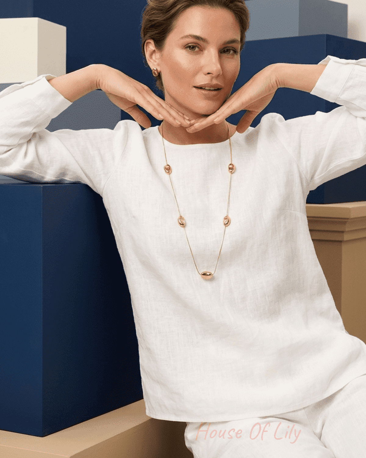 Model wears a long, modern gold chain necklace featuring polished gold bean-shaped charms over a white linen top.