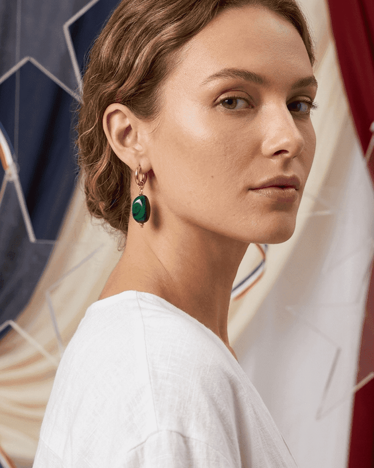 A woman wearing House of Lily's Dreamy Jelly Pebble earrings: gold hoops with smooth, green malachite-style pendants.