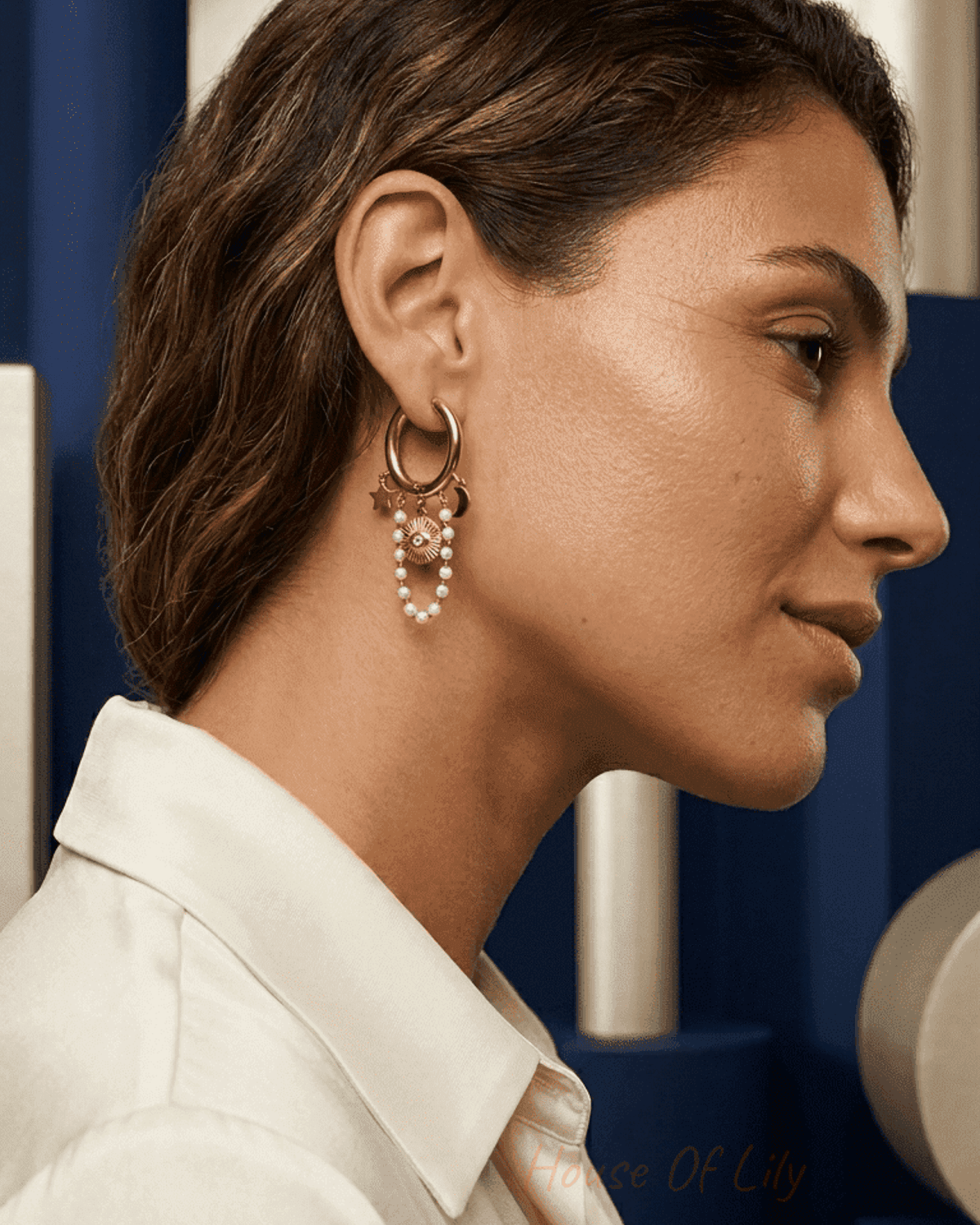 Gold hoop earrings with sun charm, moon and star accents, and dangling white pearl chains worn on a woman's ear.
