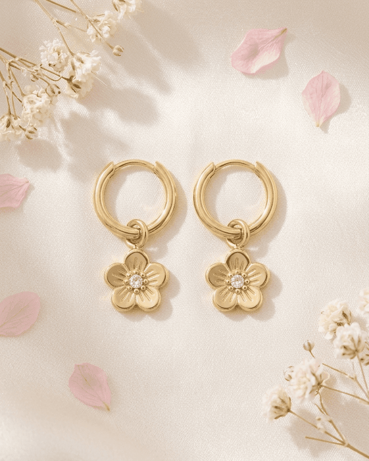 Gold hoop earrings with dainty flower pendants, featuring a central rhinestone on a light, floral-themed background.