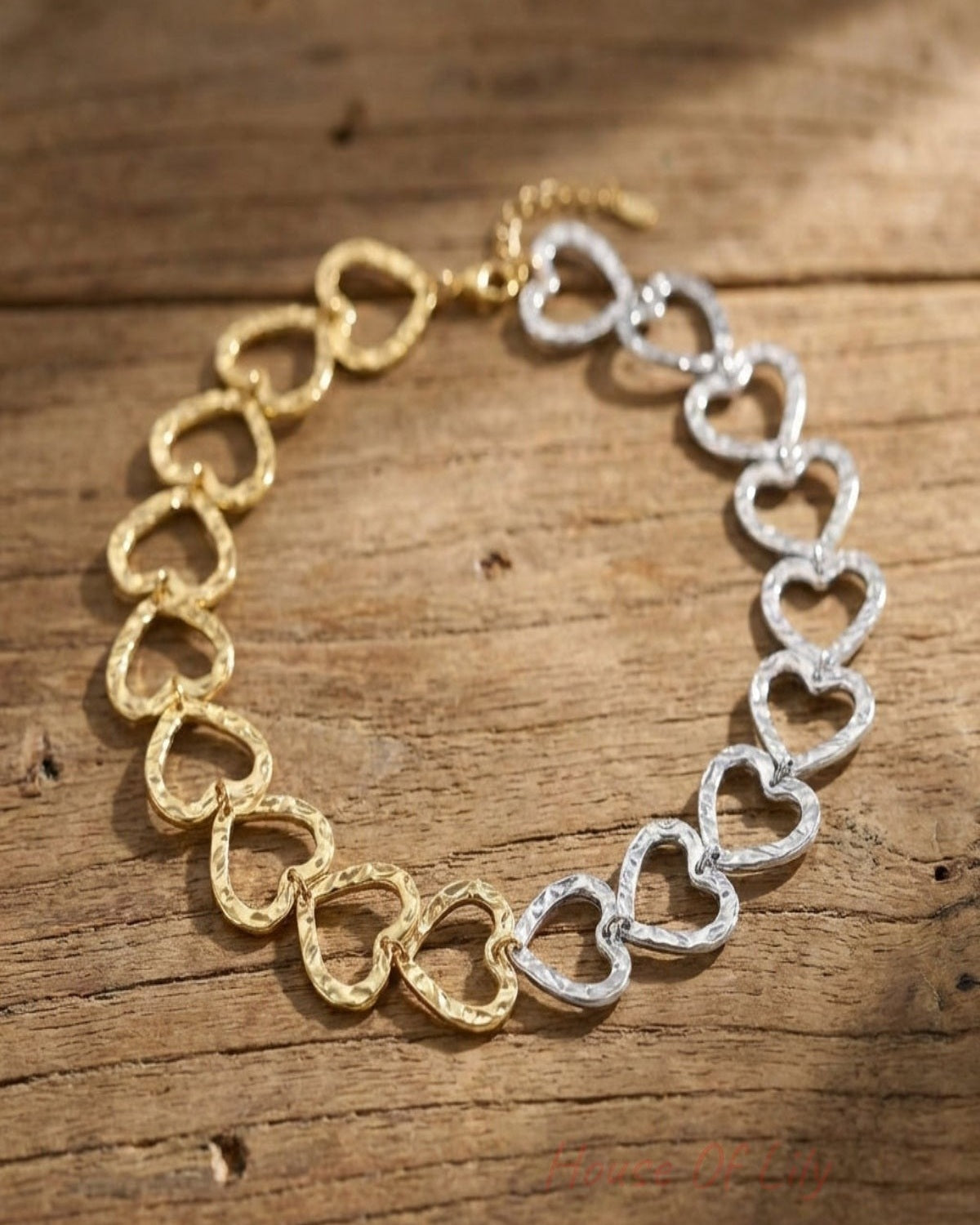 Detailed image of a small gold and silver heart link chain necklace on textured wooden surface, emphasizing fine micro-textures.