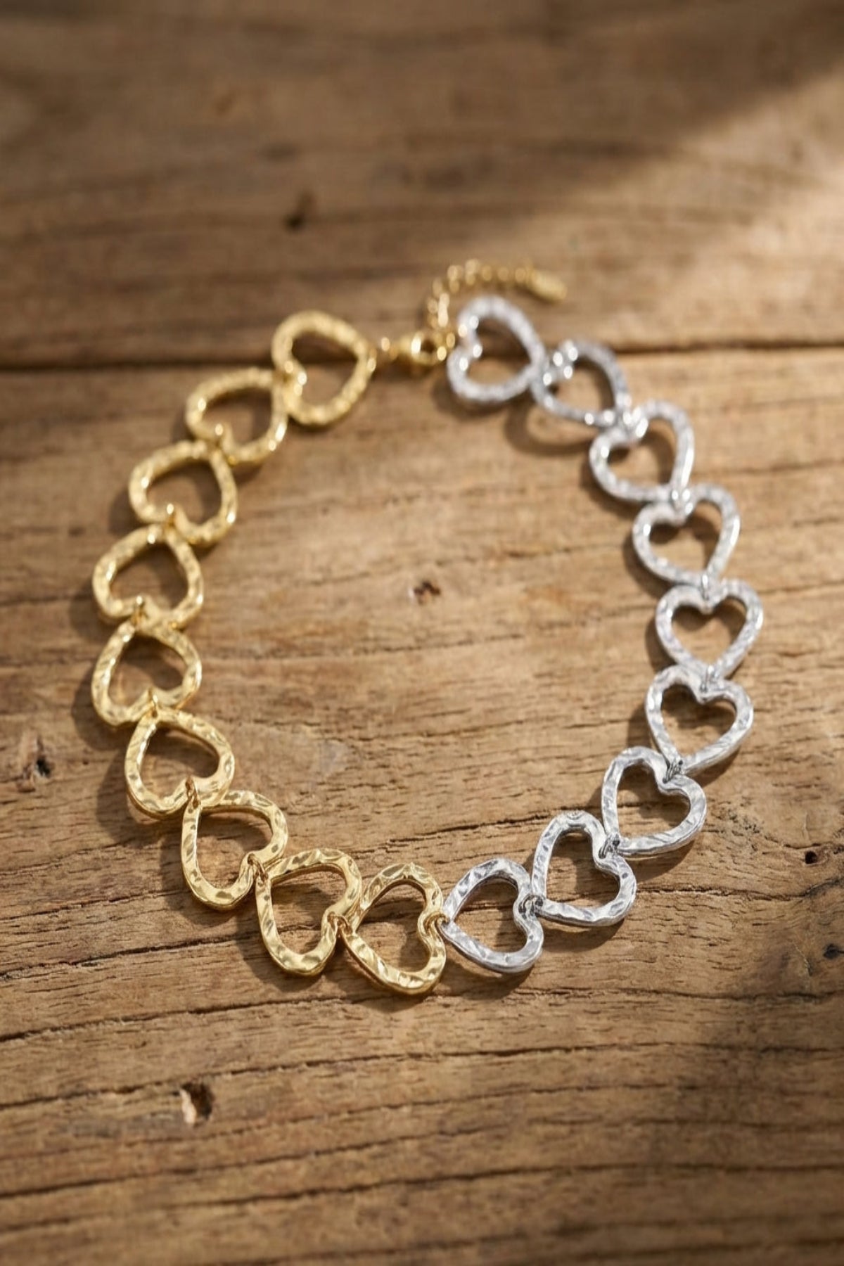 Detailed image of a small gold and silver heart link chain necklace on textured wooden surface, emphasizing fine micro-textures.