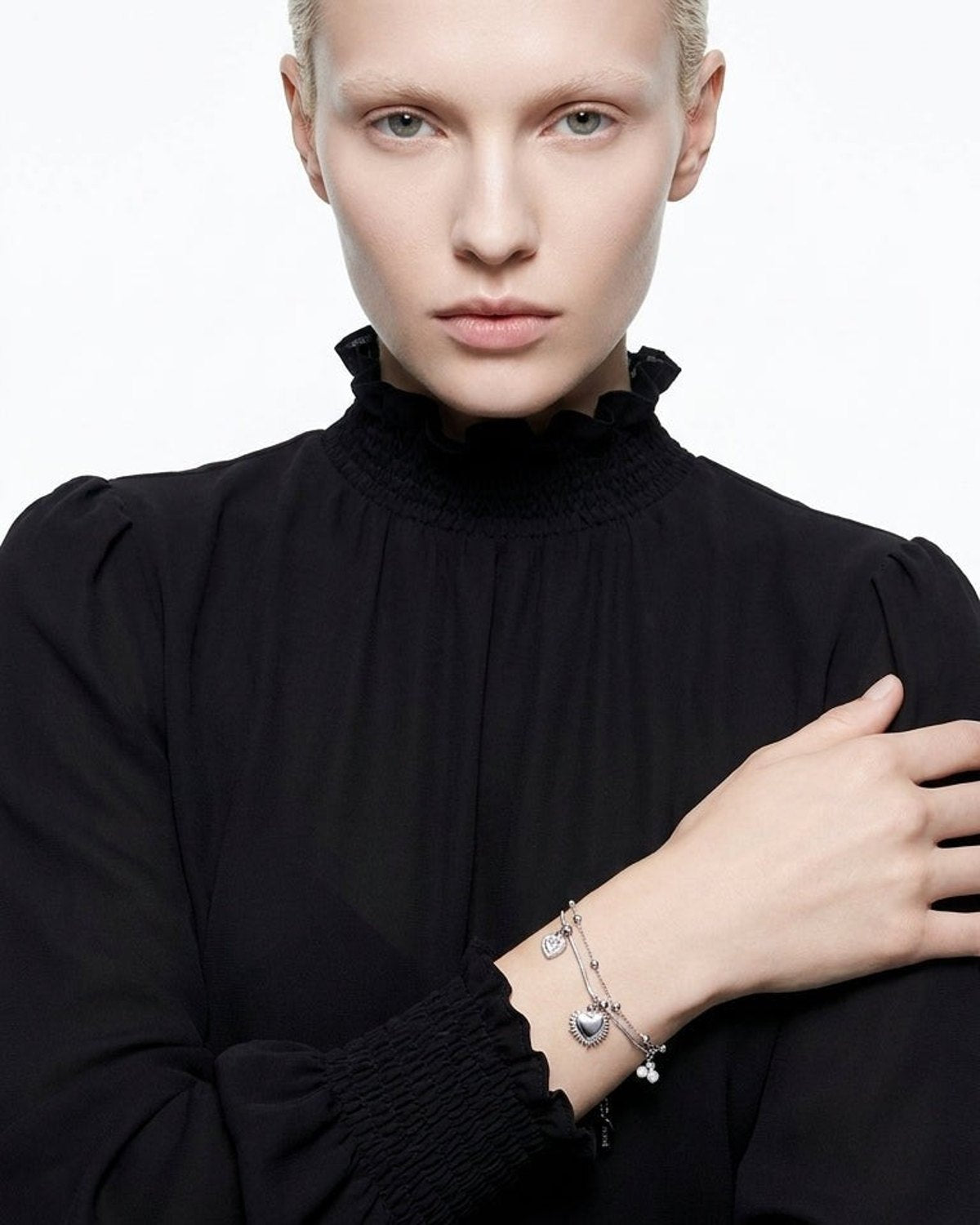 A model wearing a silver double-strand charm bracelet with heart pendants on her wrist.