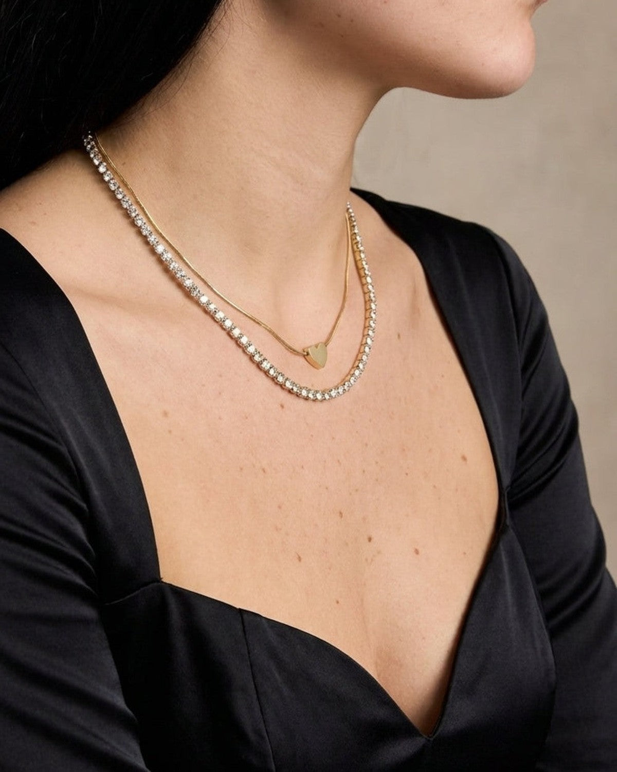 Layered gold heart necklace worn on a person, featuring a dainty heart pendant and a rhinestone tennis chain.