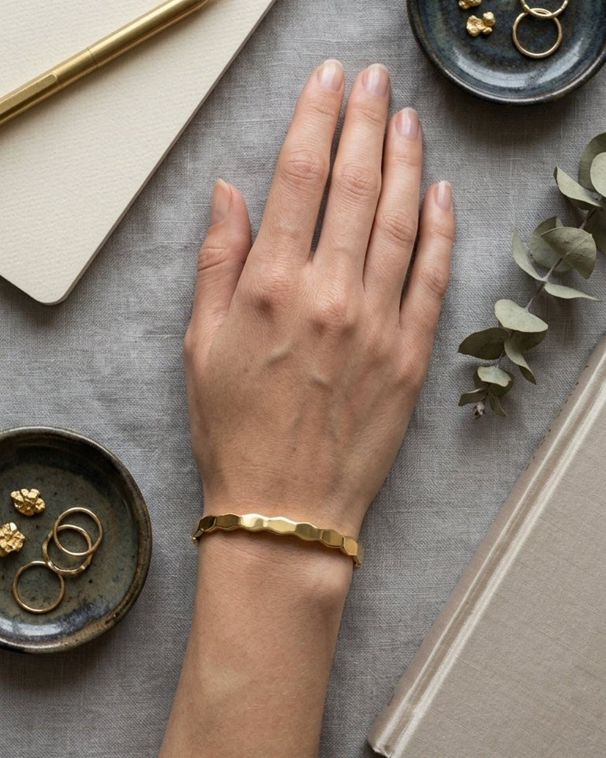 Minimalist gold bangle with a subtle, geometric, hexagonal link-style texture worn on a wrist.