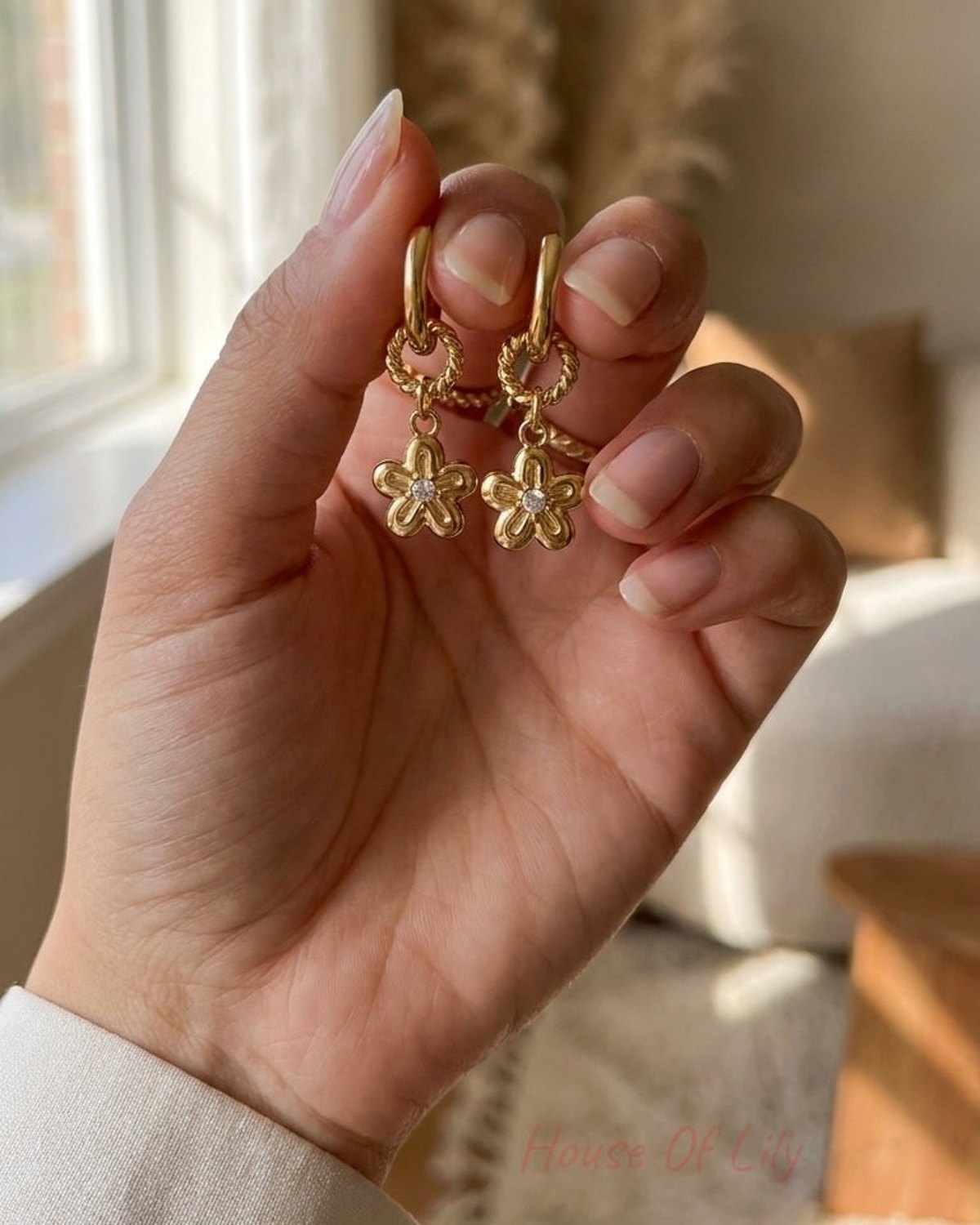 Gold huggie hoop earrings with twisted rings and daisy charms set with center cubic zirconia.
