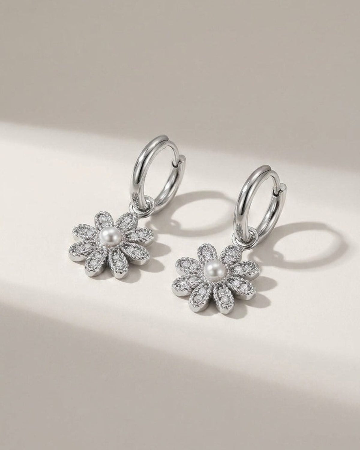 Silver hoop earrings with pavé-set flower charms featuring white pearl centers.