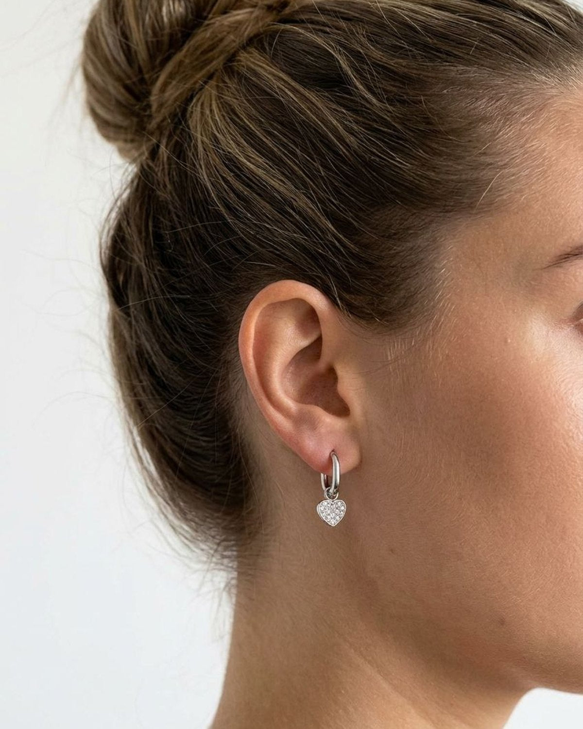 Woman wearing petite stainless steel heart drop earrings with clear pavé zircon inlay for a delicate everyday look.