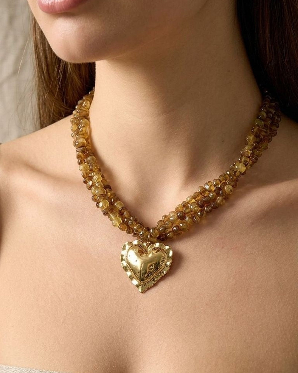 Close-up of a twisted beaded heart necklace worn on a female model's neckline, highlighting the gold-tone heart charm and acrylic beads in natural light.