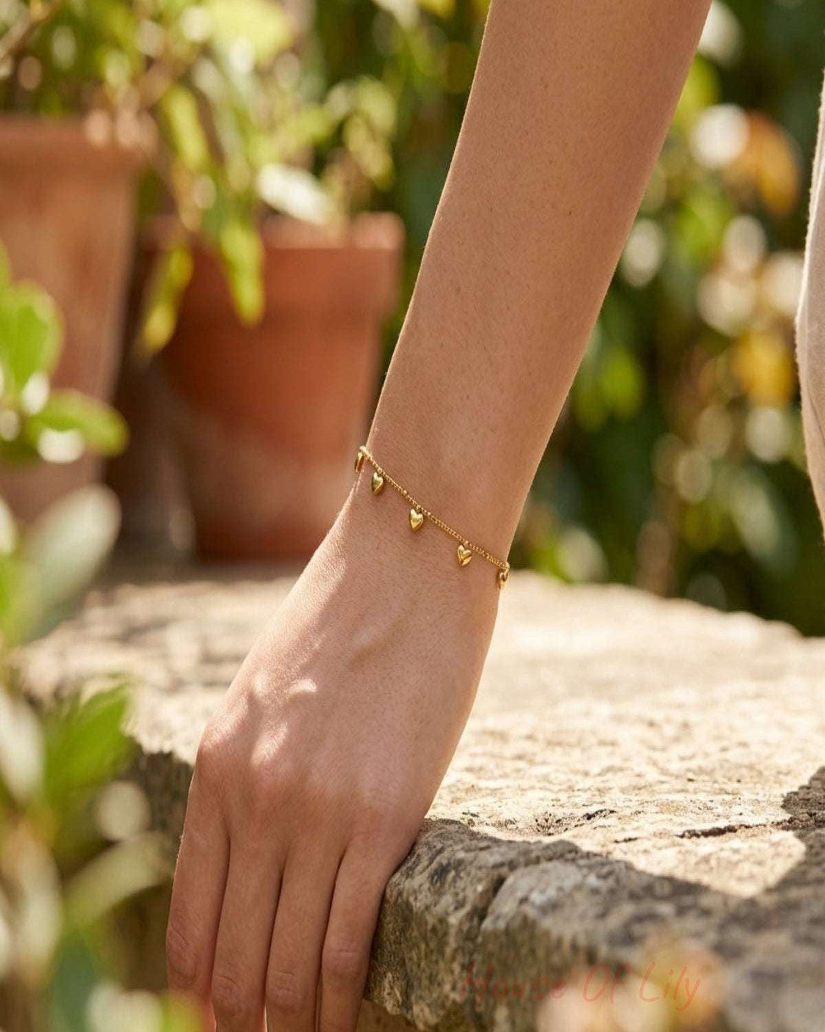 Model wearing a subtle gold-colored stainless steel bracelet with heart charms outdoors, natural daylight.