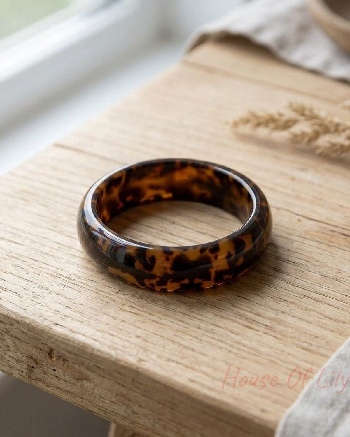 Close-up of Wild Child Leopard Bangle made of resin with animal print pattern on a natural wooden surface with soft natural lighting.