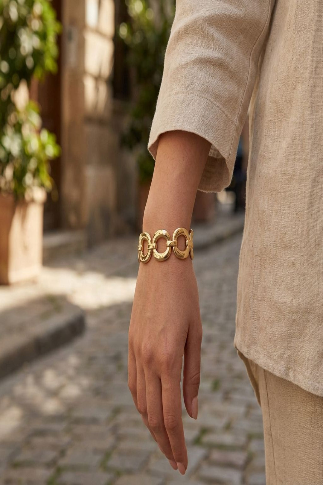 Model wearing a petite oval alloy bracelet outdoors in sunlight, showcasing its slim profile and casual, stylish appeal in an urban environment.