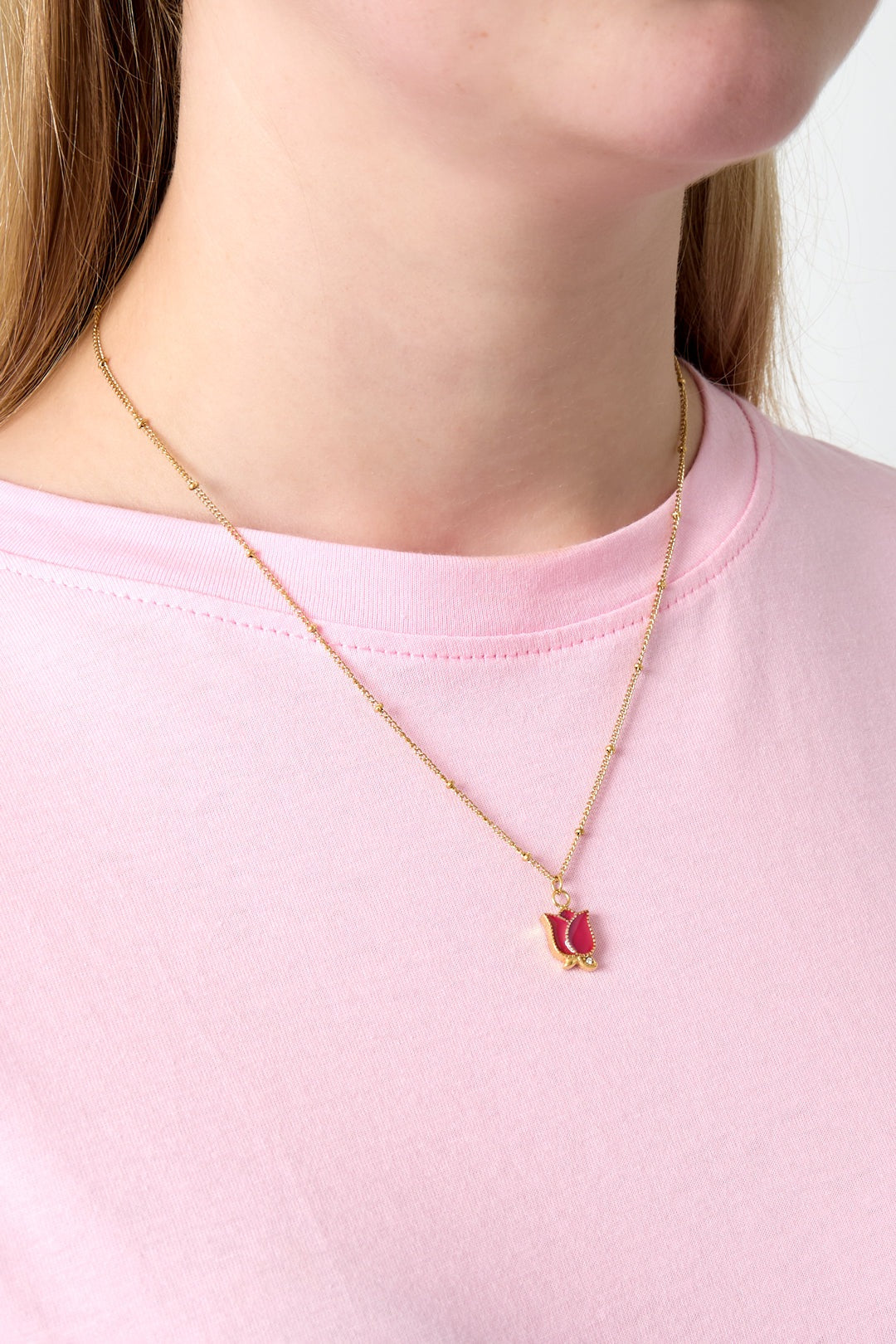 Close-up of a woman wearing a gold-tone necklace with a red enamel rose pendant over a pink t-shirt