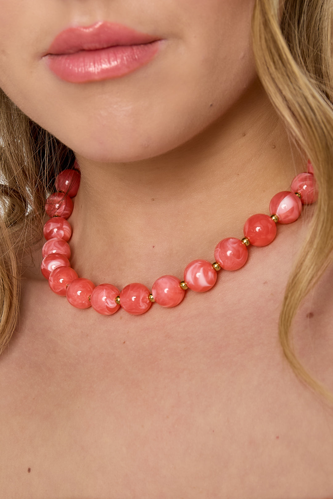 Detail shot of woman’s neck with coral pink statement necklace featuring marbled beads and gold accents