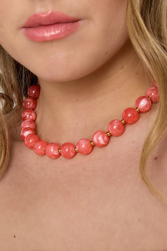 Detail shot of woman’s neck with coral pink statement necklace featuring marbled beads and gold accents