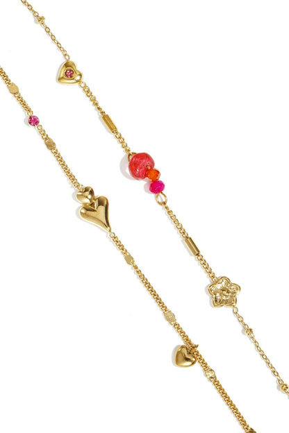 Gold chain bracelet featuring polished heart and flower charms, interspersed with pink, orange, and red accent beads.
