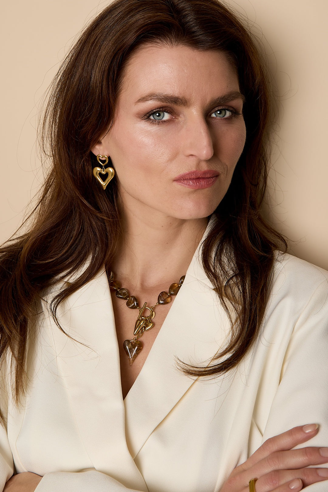 Model wearing amber brown heart bead necklace and matching gold heart earrings with cream blazer