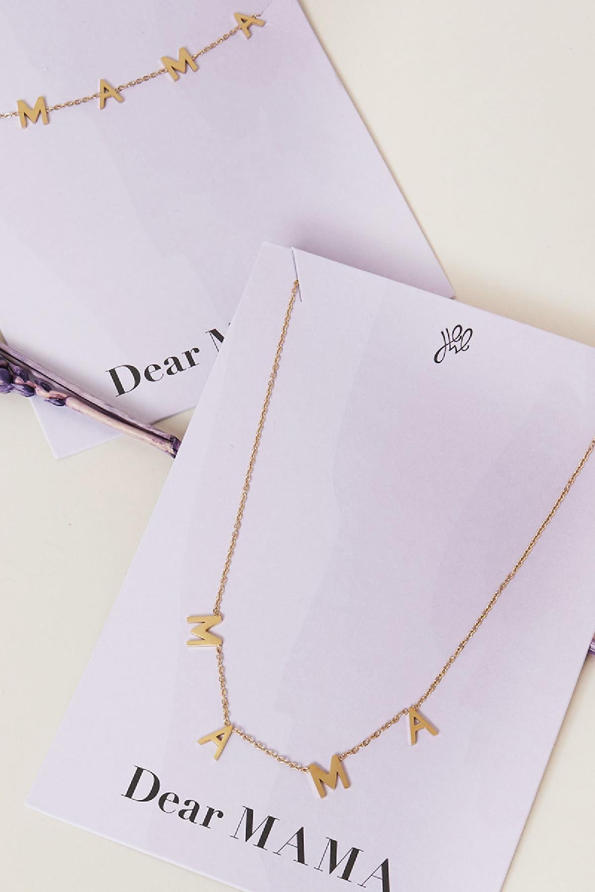 Close up of two gold tone 'MAMA' letter necklaces on white display cards, showcasing delicate chain and minimalist design