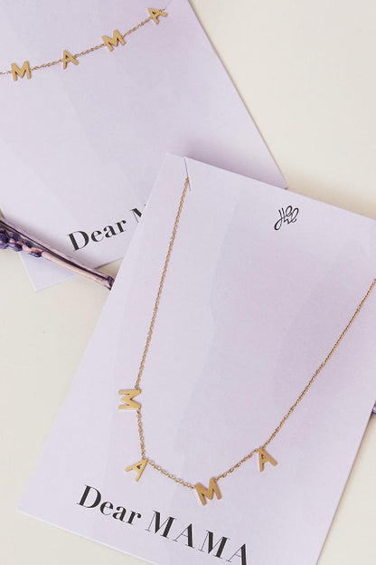 Close up of two gold tone 'MAMA' letter necklaces on white display cards, showcasing delicate chain and minimalist design