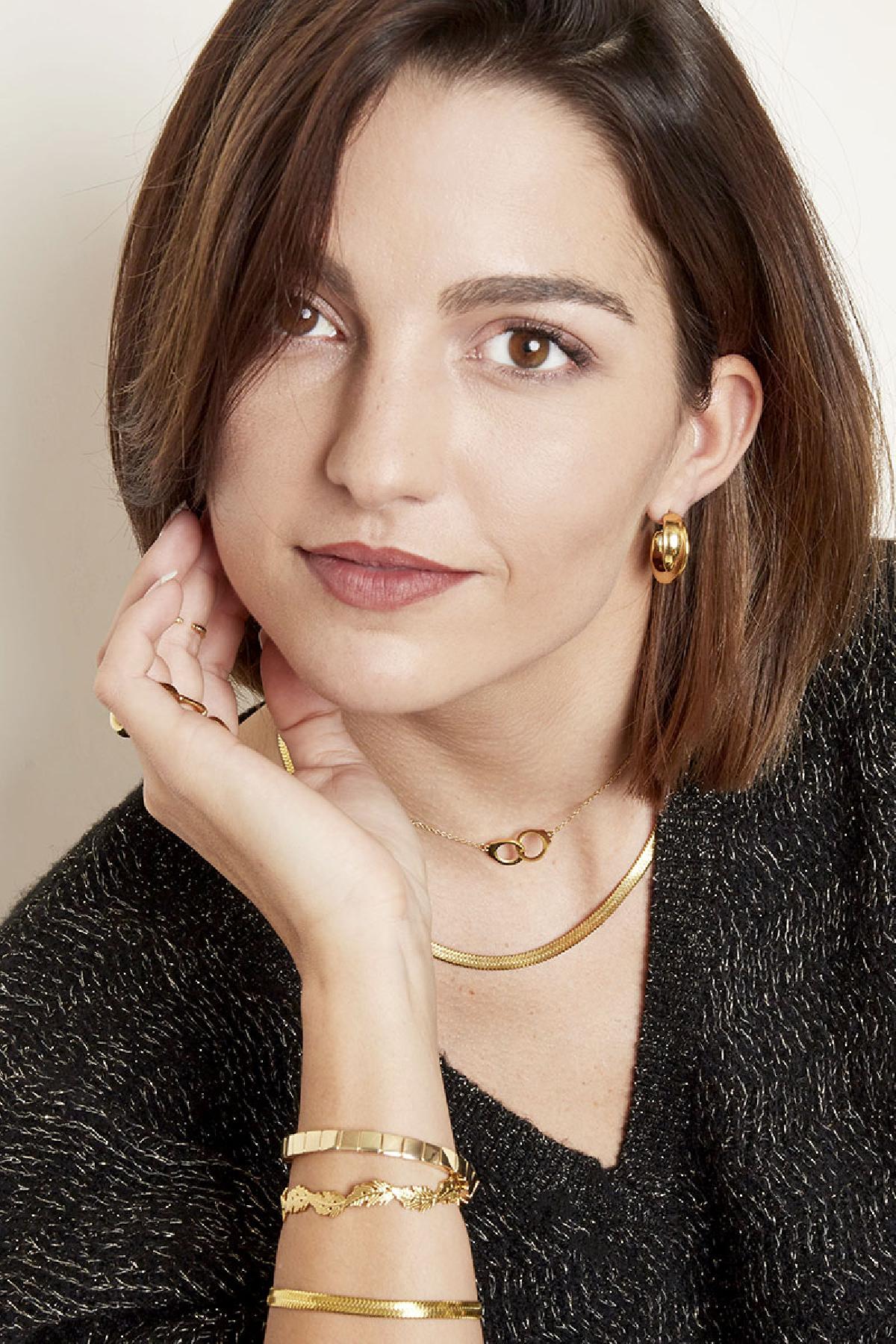 Woman wearing layered gold chain necklaces and gold hoop earrings with soft makeup and short hair
