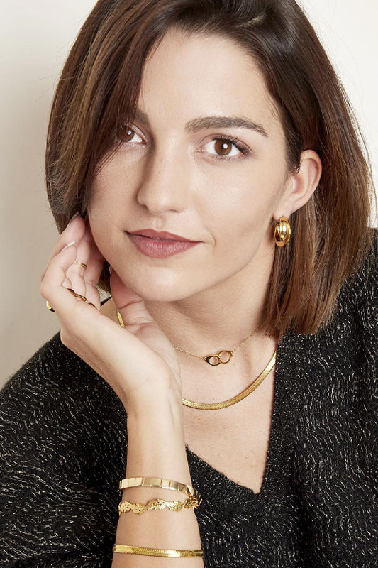 Woman wearing layered gold chain necklaces and gold hoop earrings with soft makeup and short hair