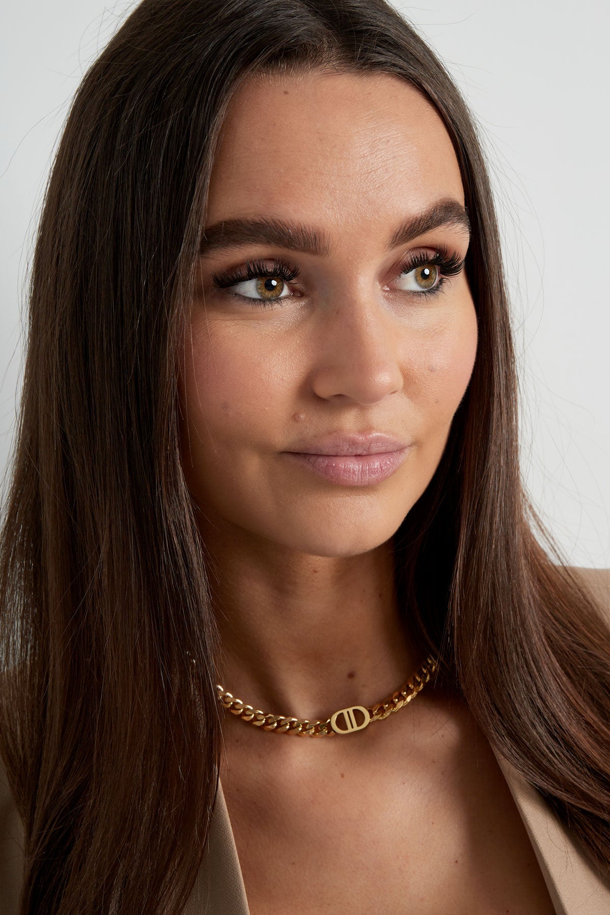 Close-up of smiling woman wearing gold chunky chain necklace with oval logo charm