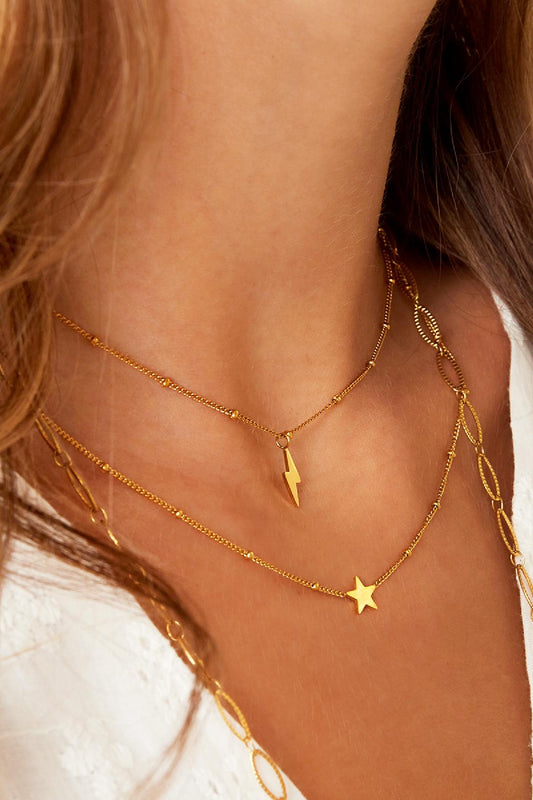 Close-up of layered gold necklaces on a woman's neck featuring a lightning bolt pendant on one chain and a star pendant on another
