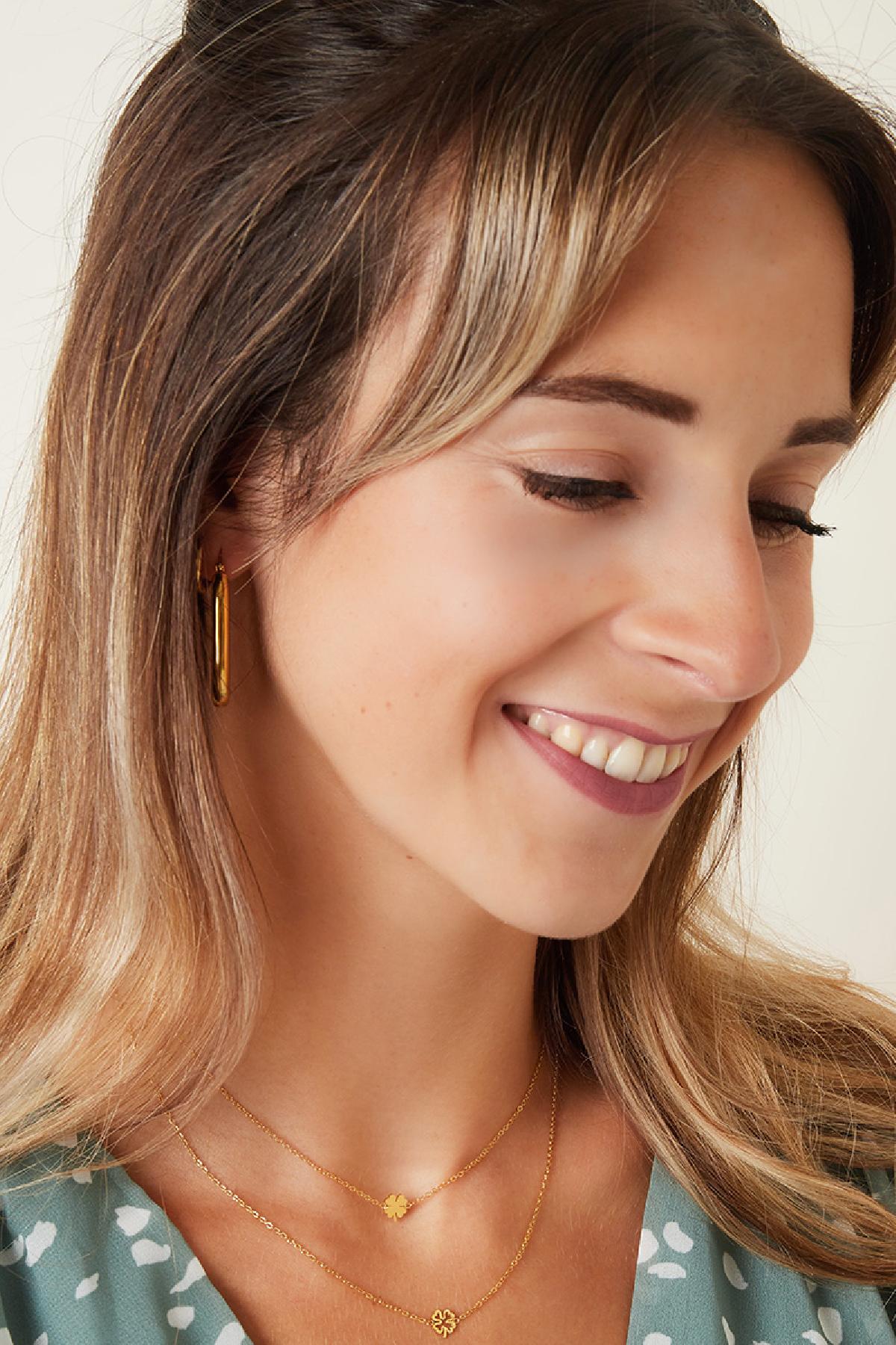 Smiling young woman wearing the gold four-leaf clover necklace paired with matching gold hoop earrings and layered necklaces